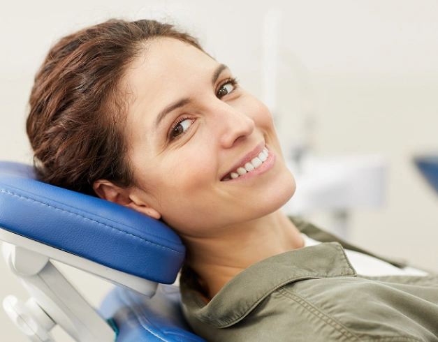 Woman smiling in dental chair wearing blue neck pillow at cosmetic dentistry office