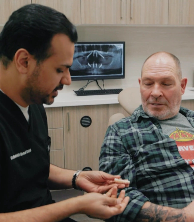 Dentist examining patient's teeth in clinical office with dental imaging display on monitor.
